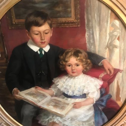 An Edwardian oil portrait painting depicting a young boy and girl reading a book together, presented within a square gilt frame featuring an oval aperture. View V