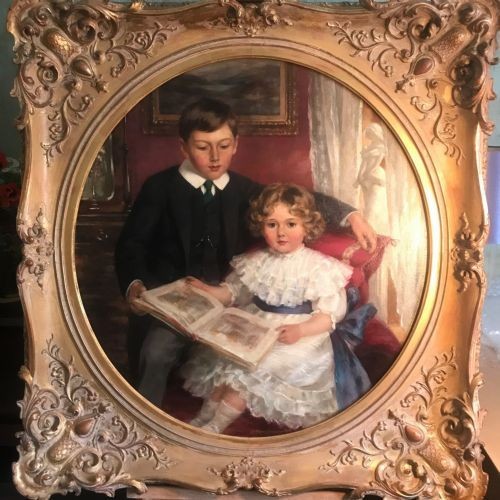 An Edwardian oil portrait painting depicting a young boy and girl reading a book together, presented within a square gilt frame featuring an oval aperture. View XIV