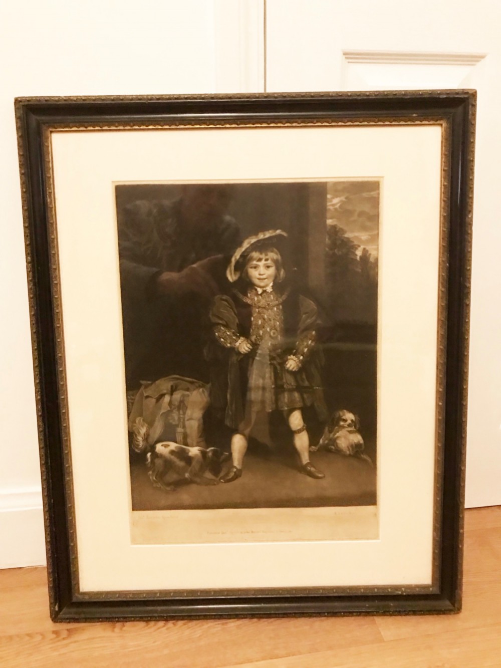 A framed monochrome mezzotint print depicting a young boy in Tudor attire styled as Henry VIII flanked by two small dogs. View IV