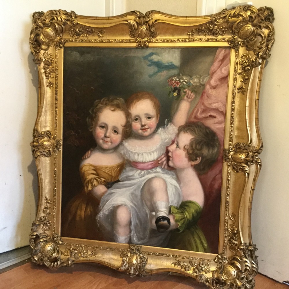 A 19th-century oil portrait of three children in classical attire contained within a carved swept giltwood frame.