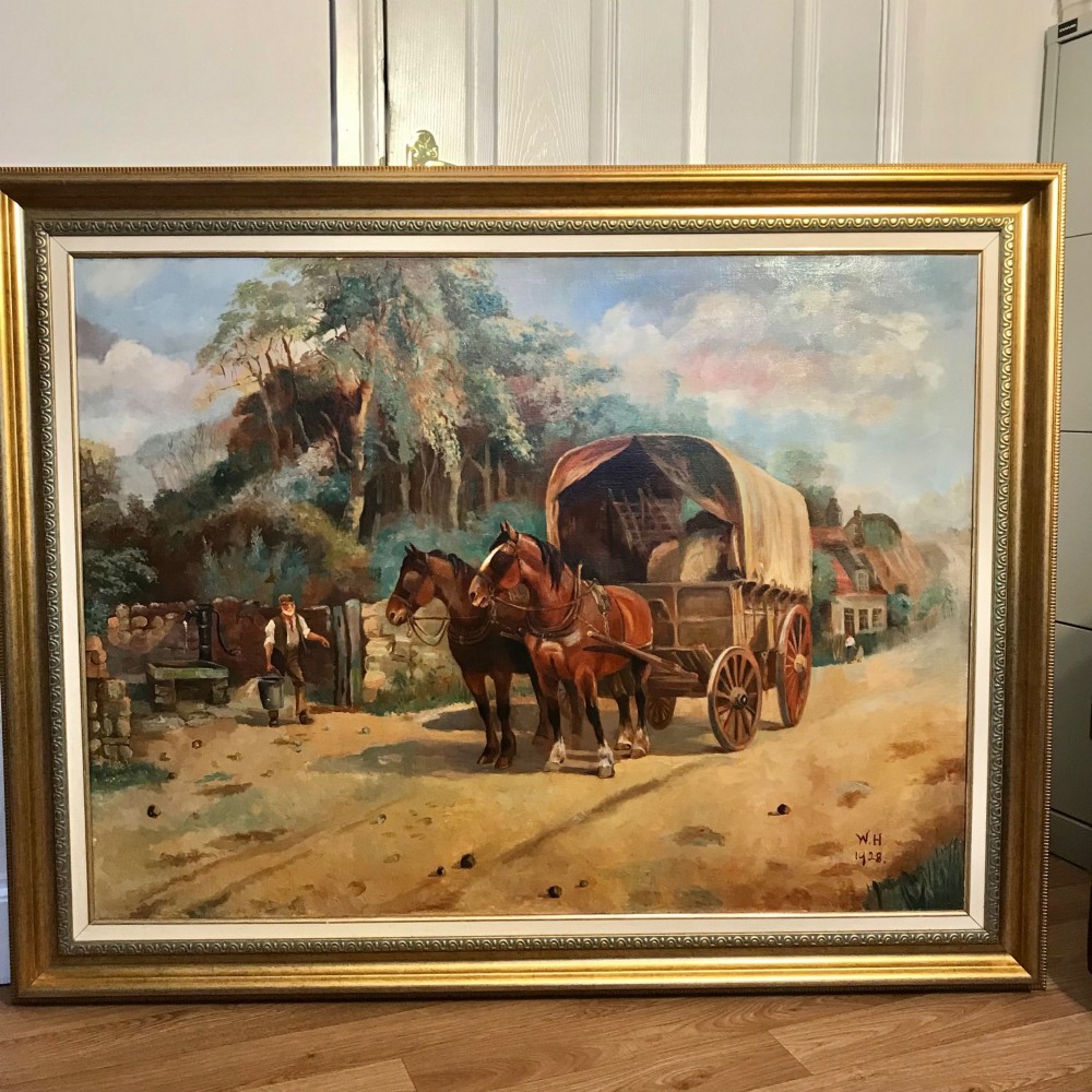 A framed oil painting depicting two brown draught horses harnessed to a covered wagon along a rural dirt road near cottages and trees.