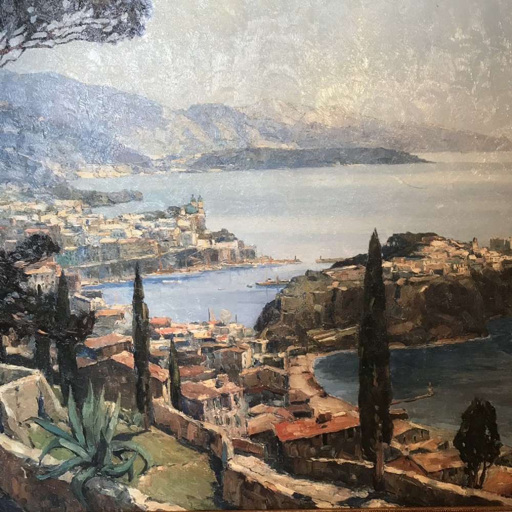 A large framed landscape print depicting a coastal vista of Monaco with cypress trees and stone walls overlooking the sea, set within a gilded frame. View X