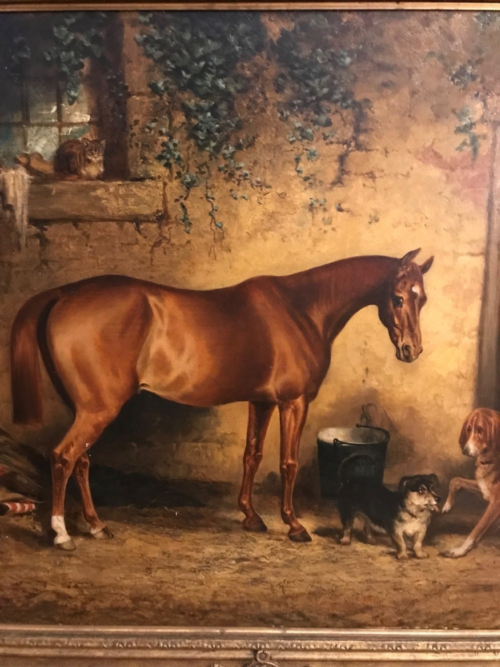 A 19th-century oil painting on canvas portraying a brown bay hunter horse inside a stone stable with two dogs, presented in an ornate gilt frame. View IV
