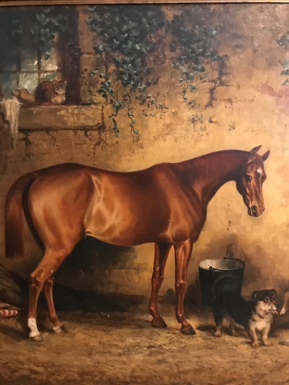 A 19th-century oil painting on canvas portraying a brown bay hunter horse inside a stone stable with two dogs, presented in an ornate gilt frame. View VII
