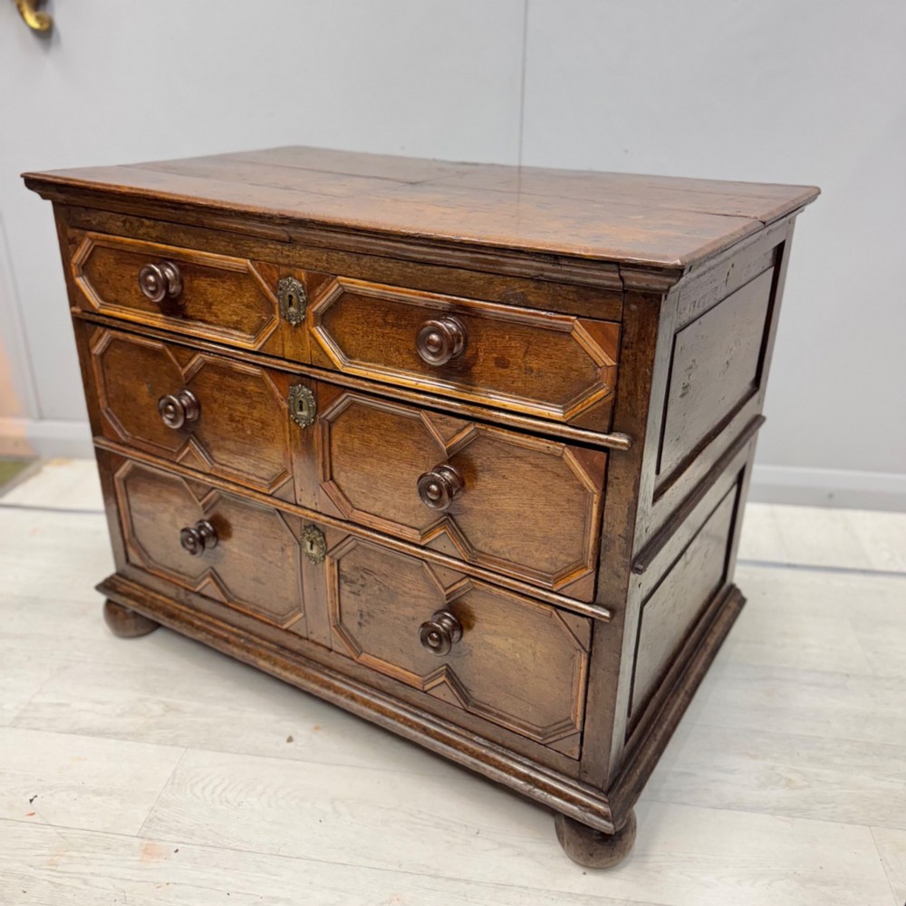 A 17th-century dark oak chest of drawers featuring geometric mitred mouldings on three drawer fronts, turned wooden handles, brass escutcheons, and bun feet. View II