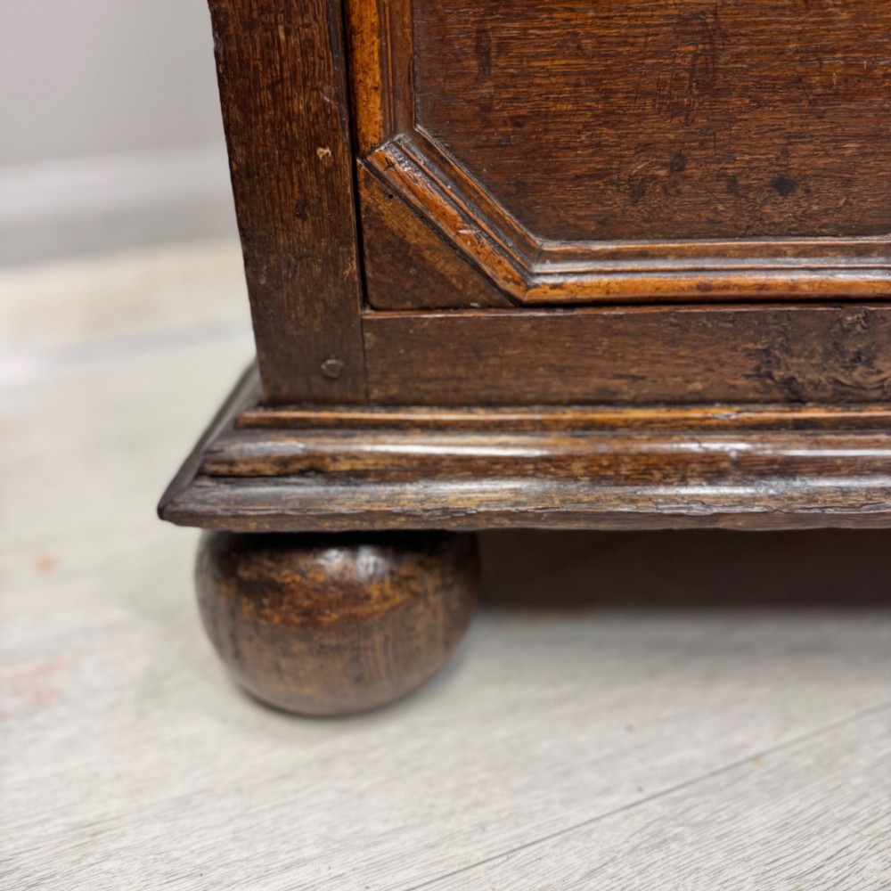 A 17th-century dark oak chest of drawers featuring geometric mitred mouldings on three drawer fronts, turned wooden handles, brass escutcheons, and bun feet. View XI