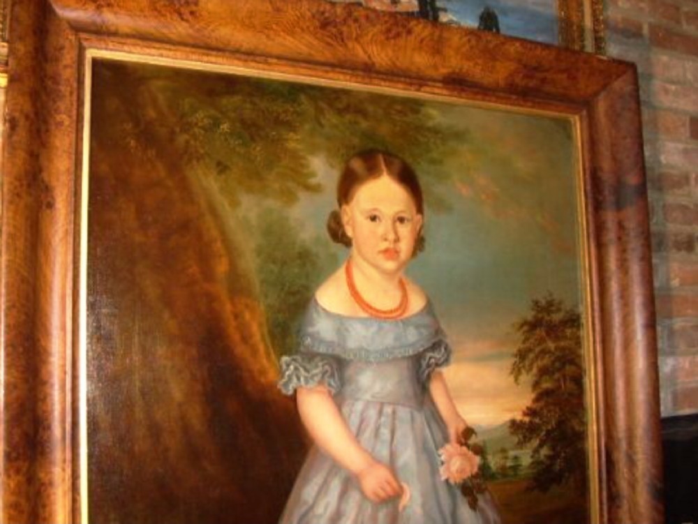An antique oil portrait on canvas depicting a young girl in a blue dress holding a rose, displayed within a wide flame wood frame. View II