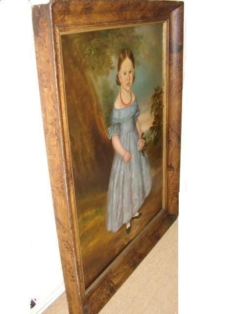 An antique oil portrait on canvas depicting a young girl in a blue dress holding a rose, displayed within a wide flame wood frame. View IV