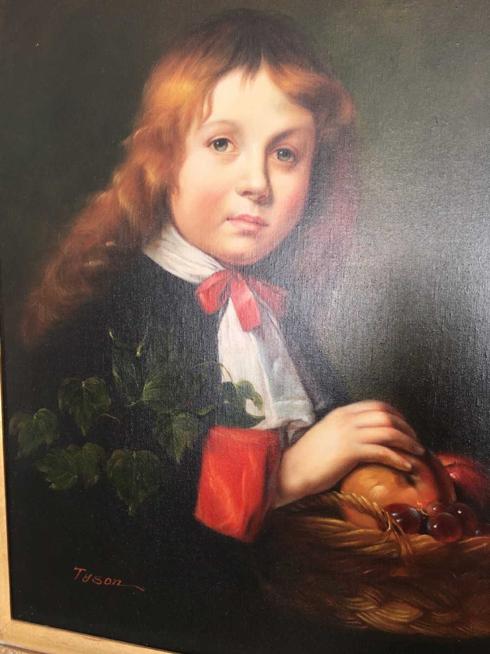A framed portrait of a young boy with reddish-brown hair holding a basket of fruit, set within an ornate gilded frame. View II