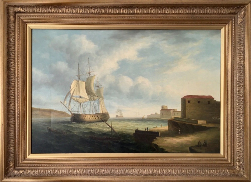 A 19th-century style marine oil painting on panel depicting a large sailing warship anchored near a stone coastal fortification under a cloudy sky, presented in a heavily moulded gold gilt frame.