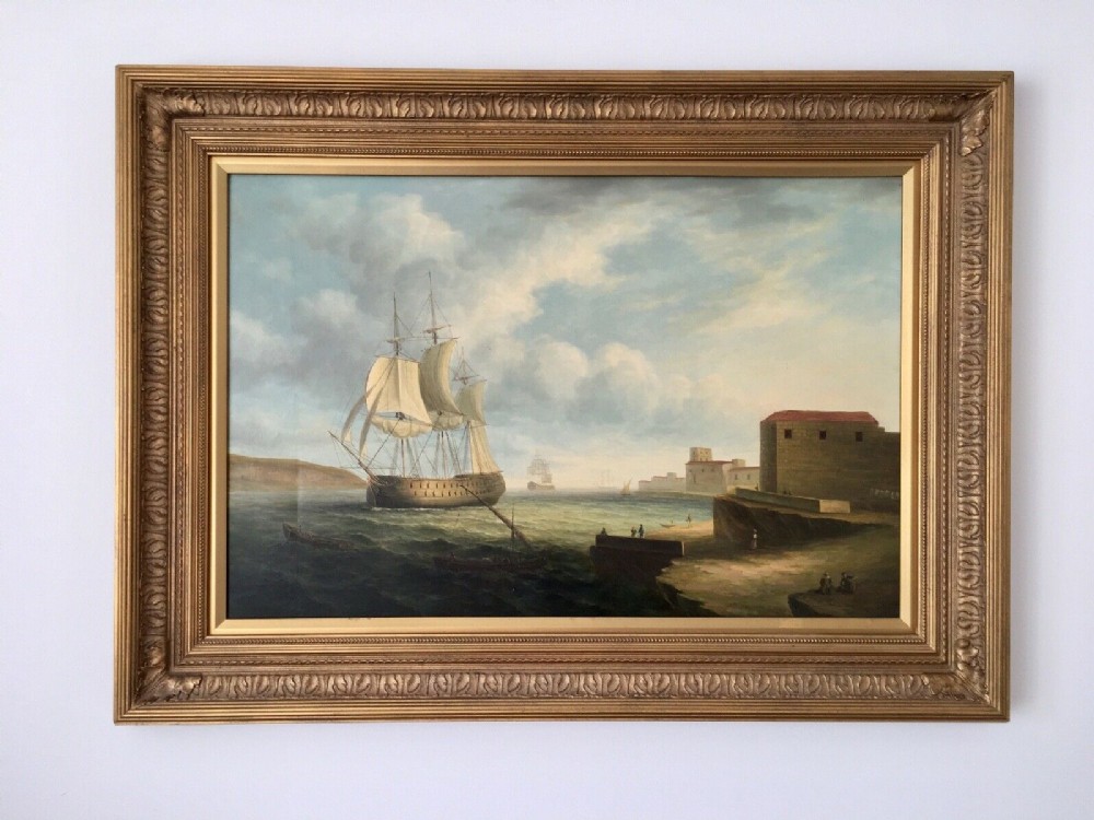 A 19th-century style marine oil painting on panel depicting a large sailing warship anchored near a stone coastal fortification under a cloudy sky, presented in a heavily moulded gold gilt frame. View III