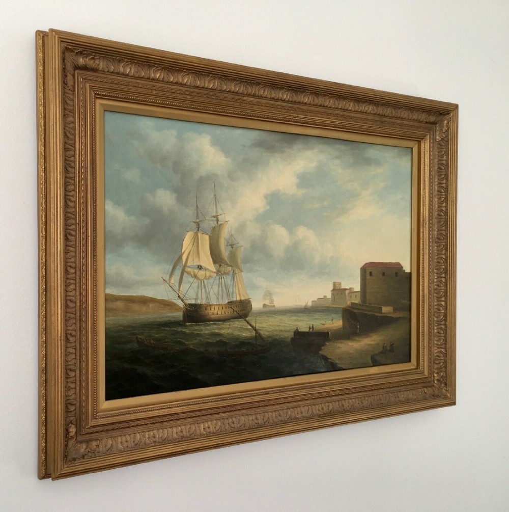 A 19th-century style marine oil painting on panel depicting a large sailing warship anchored near a stone coastal fortification under a cloudy sky, presented in a heavily moulded gold gilt frame. View IV