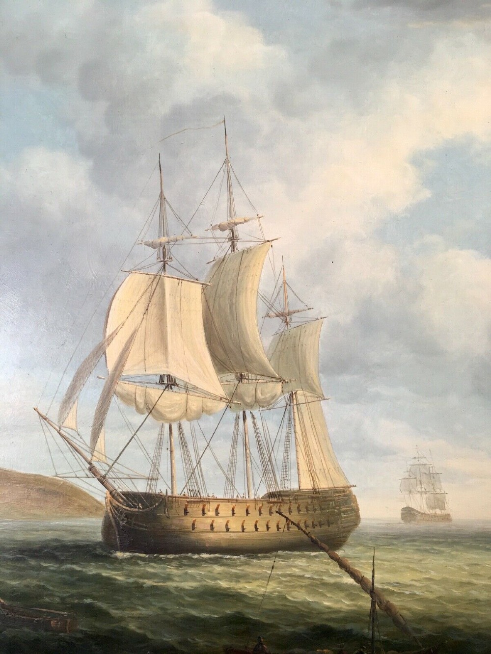 A 19th-century style marine oil painting on panel depicting a large sailing warship anchored near a stone coastal fortification under a cloudy sky, presented in a heavily moulded gold gilt frame. View V