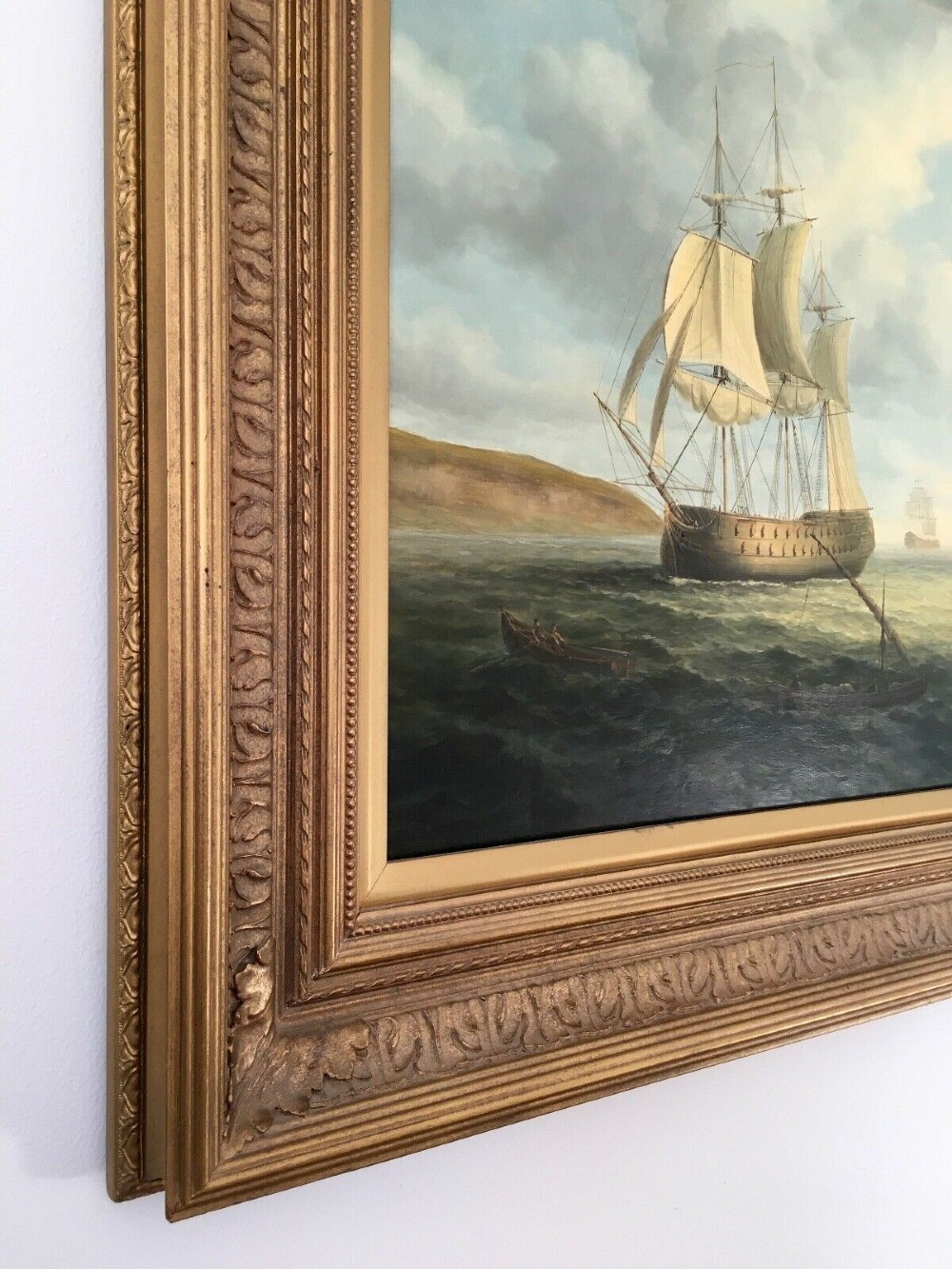 A 19th-century style marine oil painting on panel depicting a large sailing warship anchored near a stone coastal fortification under a cloudy sky, presented in a heavily moulded gold gilt frame. View VII