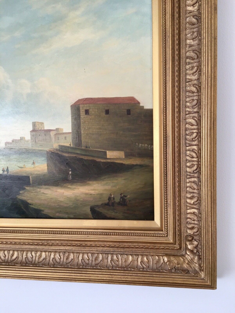 A 19th-century style marine oil painting on panel depicting a large sailing warship anchored near a stone coastal fortification under a cloudy sky, presented in a heavily moulded gold gilt frame. View VIII