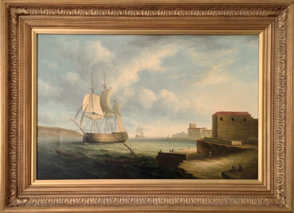A 19th-century style marine oil painting on panel depicting a large sailing warship anchored near a stone coastal fortification under a cloudy sky, presented in a heavily moulded gold gilt frame. View XII