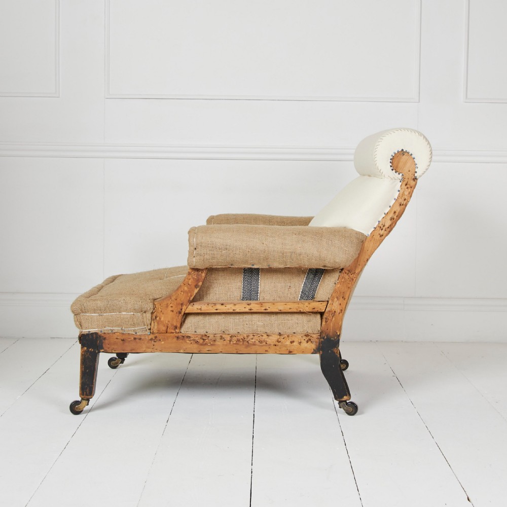 A Victorian scroll-back armchair featuring exposed deconstructed hessian upholstery, a cream fabric back roll, turned dark legs, and brass castors. View II
