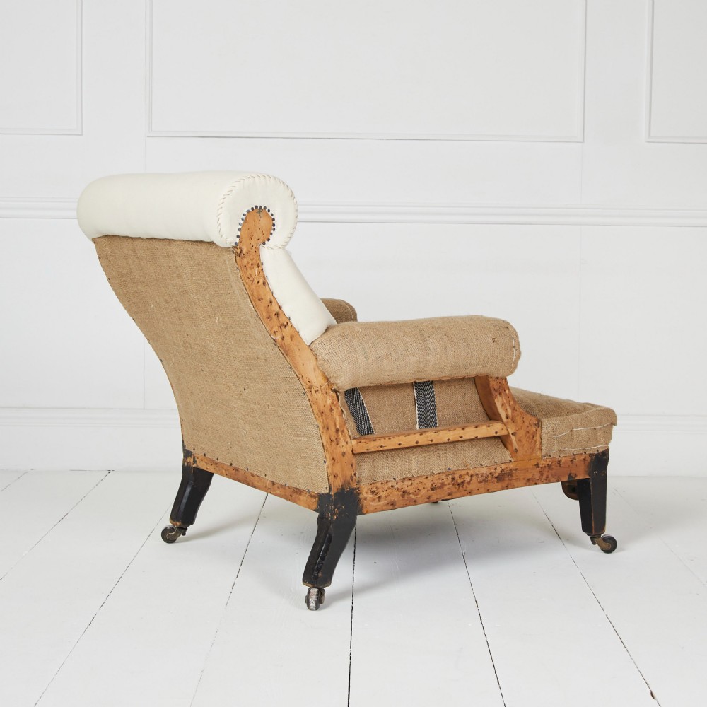 A Victorian scroll-back armchair featuring exposed deconstructed hessian upholstery, a cream fabric back roll, turned dark legs, and brass castors. View IV
