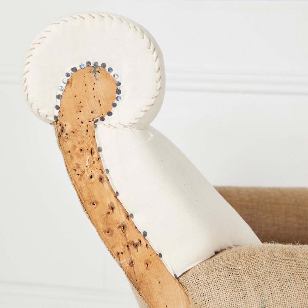 A Victorian scroll-back armchair featuring exposed deconstructed hessian upholstery, a cream fabric back roll, turned dark legs, and brass castors. View V