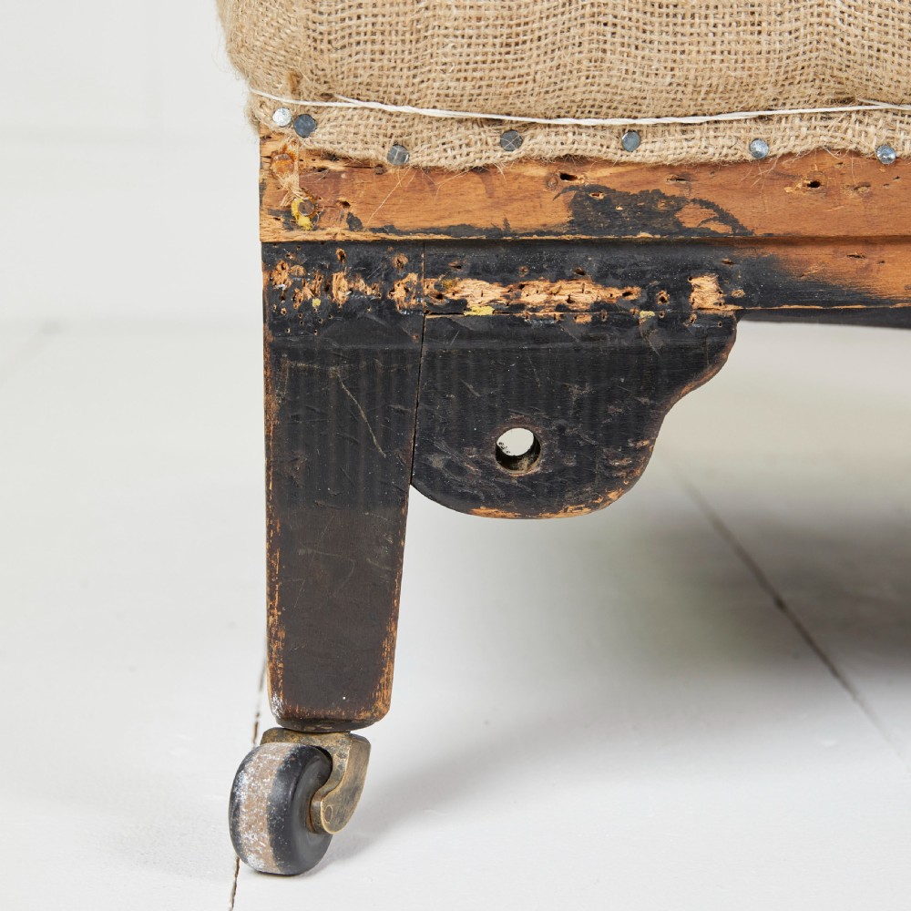 A Victorian scroll-back armchair featuring exposed deconstructed hessian upholstery, a cream fabric back roll, turned dark legs, and brass castors. View VI