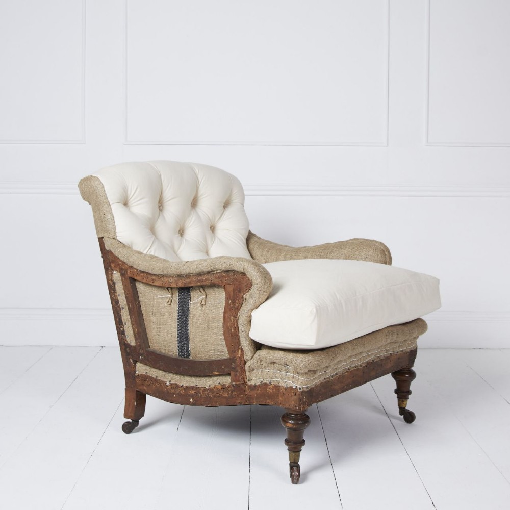 A Victorian Howard style armchair upholstered in natural calico and hessian with deep-tufted buttoning, turned front legs, and brass castors.