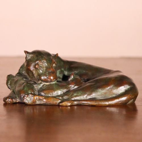 fig 1. A cast bronze sculpture depicting a recumbent lioness with a dark green verdigris patina resting on a flat surface.