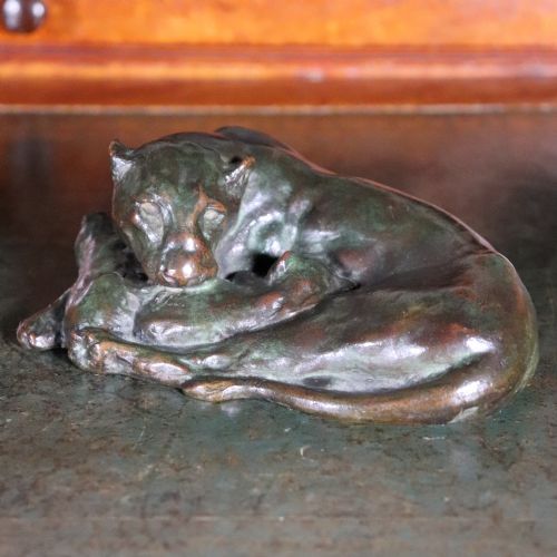 fig 3. A cast bronze sculpture depicting a recumbent lioness with a dark green verdigris patina resting on a flat surface.