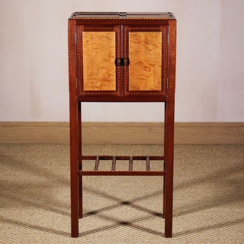 fig 2. A tall mahogany cabinet on stand featuring contrasting light wood door panels with inlaid stringing borders and a slatted lower shelf.