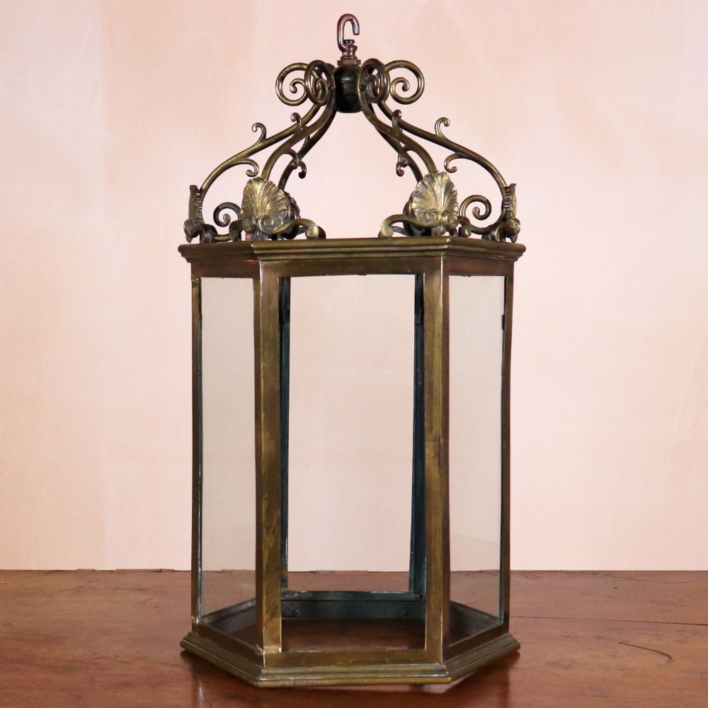 An antique hexagonal bronze hall lantern featuring glazed glass panels, acanthus leaf accents, and a scrolled canopy frame.