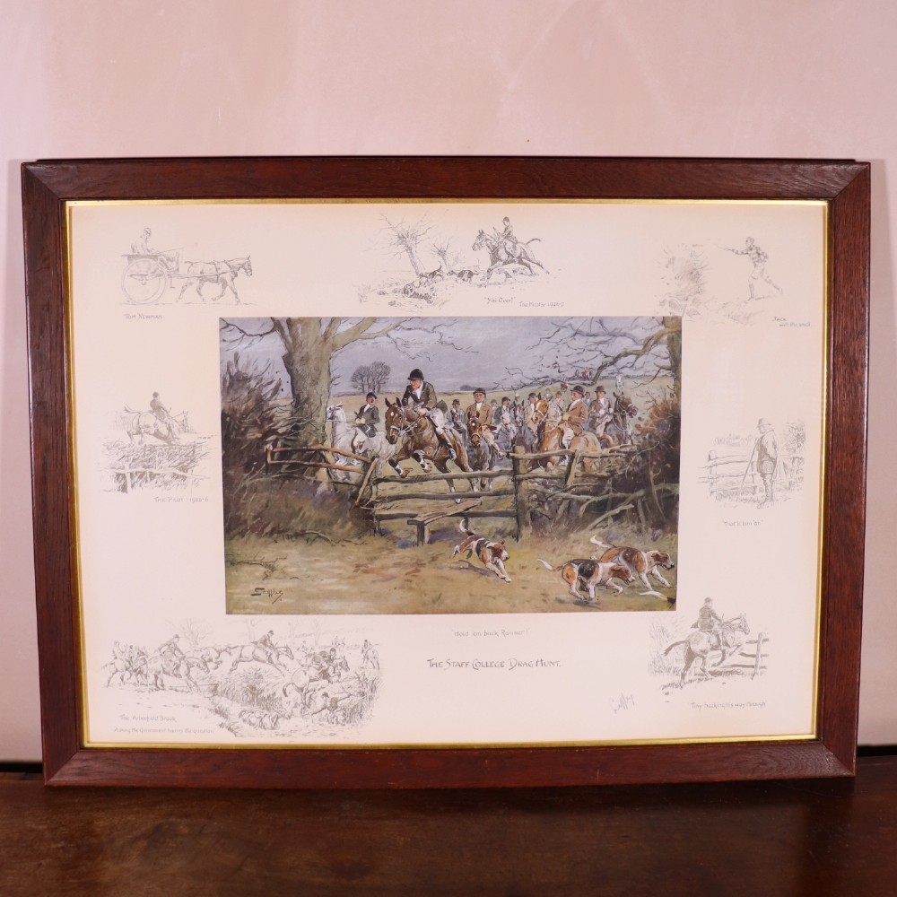 A framed antique equestrian print titled The Staff College Drag Hunt by Snaffles featuring horses and hounds jumping a wooden fence surrounded by monochrome vignettes in a dark oak frame.
