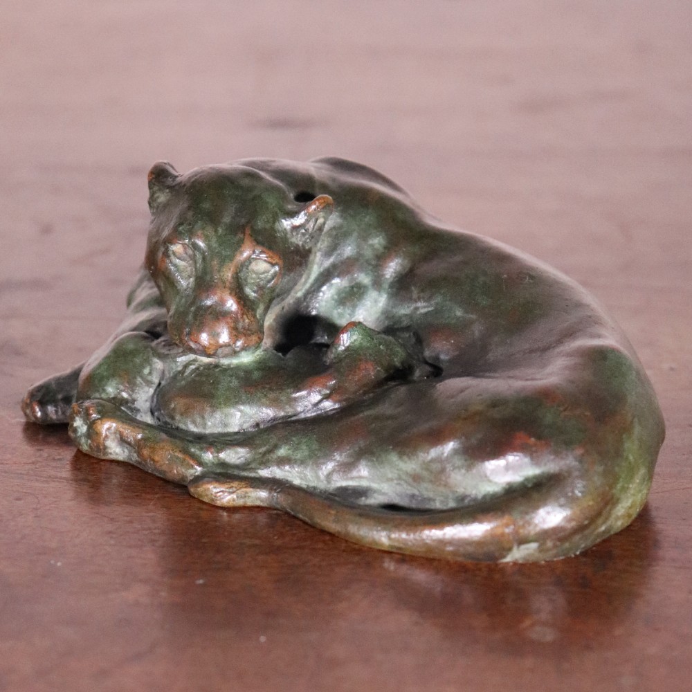 A cast bronze sculpture depicting a recumbent lioness with a dark green verdigris patina resting on a flat surface.