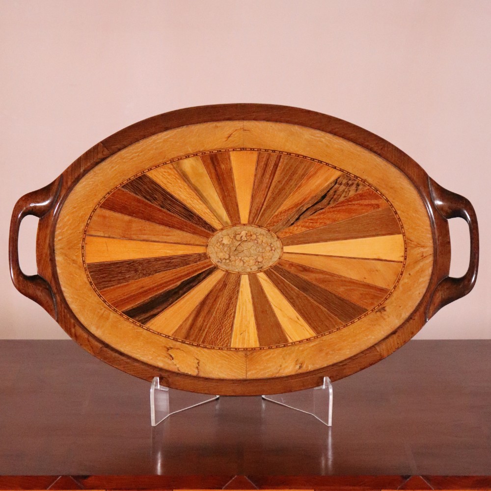 An oval antique tray featuring a central sunburst parquetry design of contrasting specimen woods with carved side handles.
