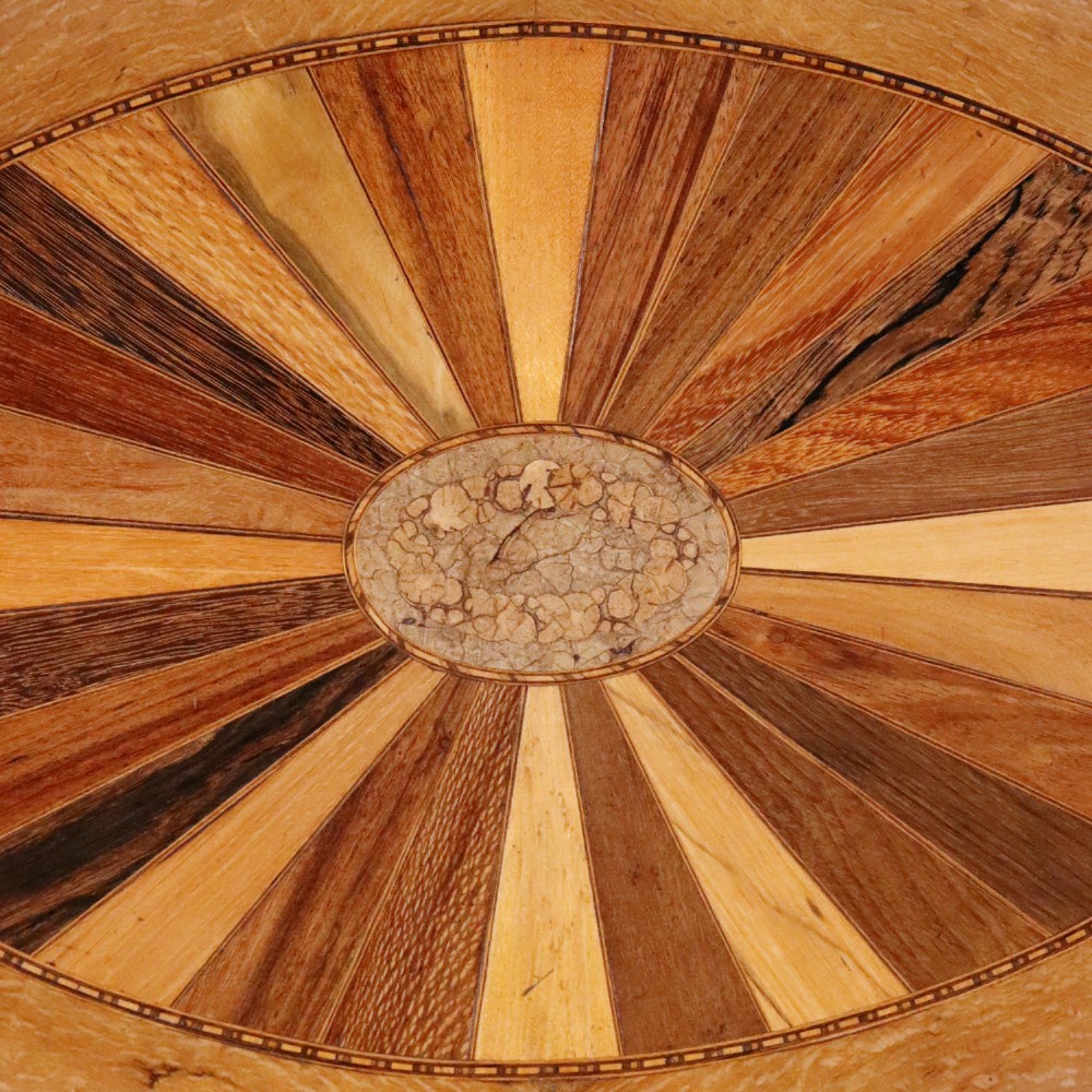 An oval antique tray featuring a central sunburst parquetry design of contrasting specimen woods with carved side handles. View II