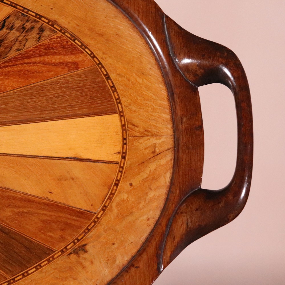An oval antique tray featuring a central sunburst parquetry design of contrasting specimen woods with carved side handles. View III