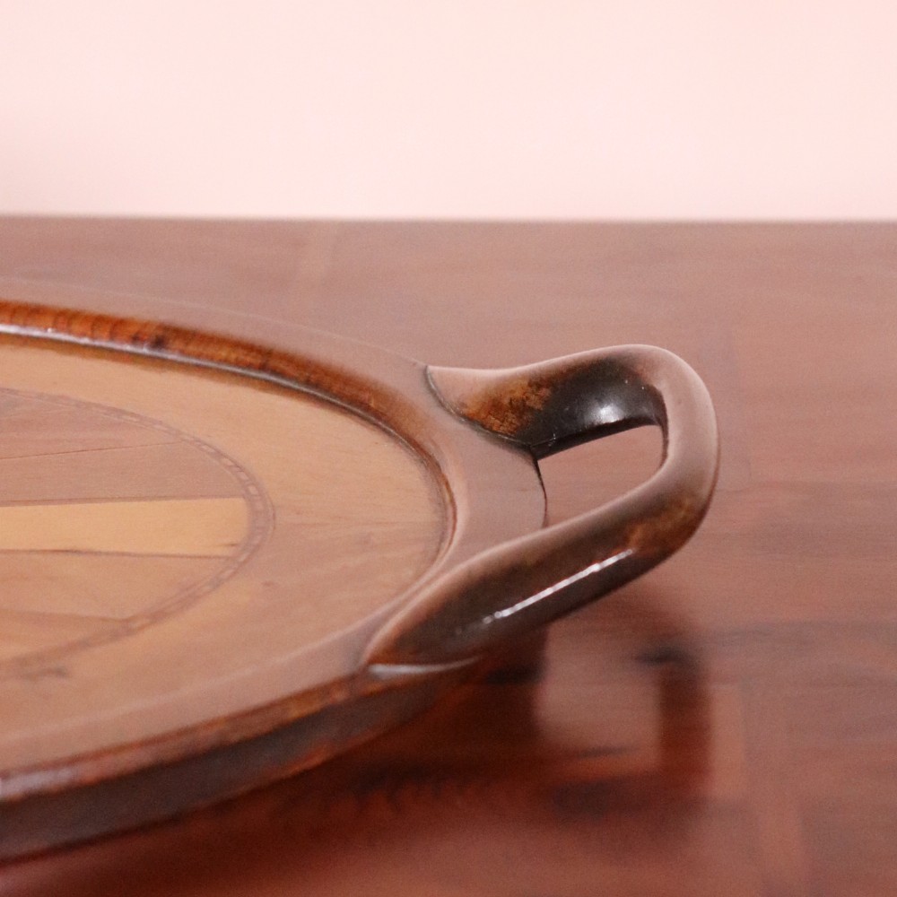 An oval antique tray featuring a central sunburst parquetry design of contrasting specimen woods with carved side handles. View VII
