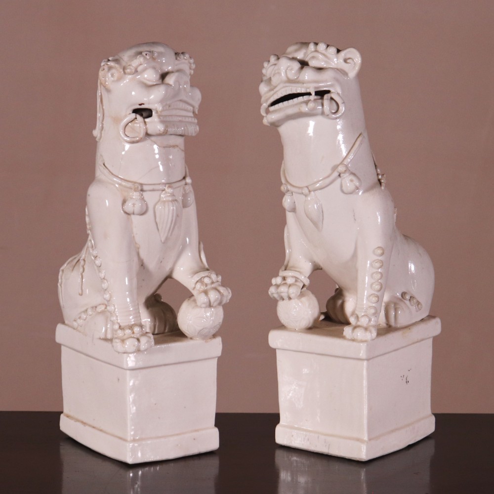 A pair of 18th-century cream-glazed Blanc de Chine porcelain guardian lion statues seated upright on rectangular bases.