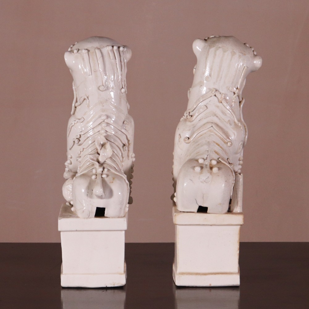 A pair of 18th-century cream-glazed Blanc de Chine porcelain guardian lion statues seated upright on rectangular bases. View II