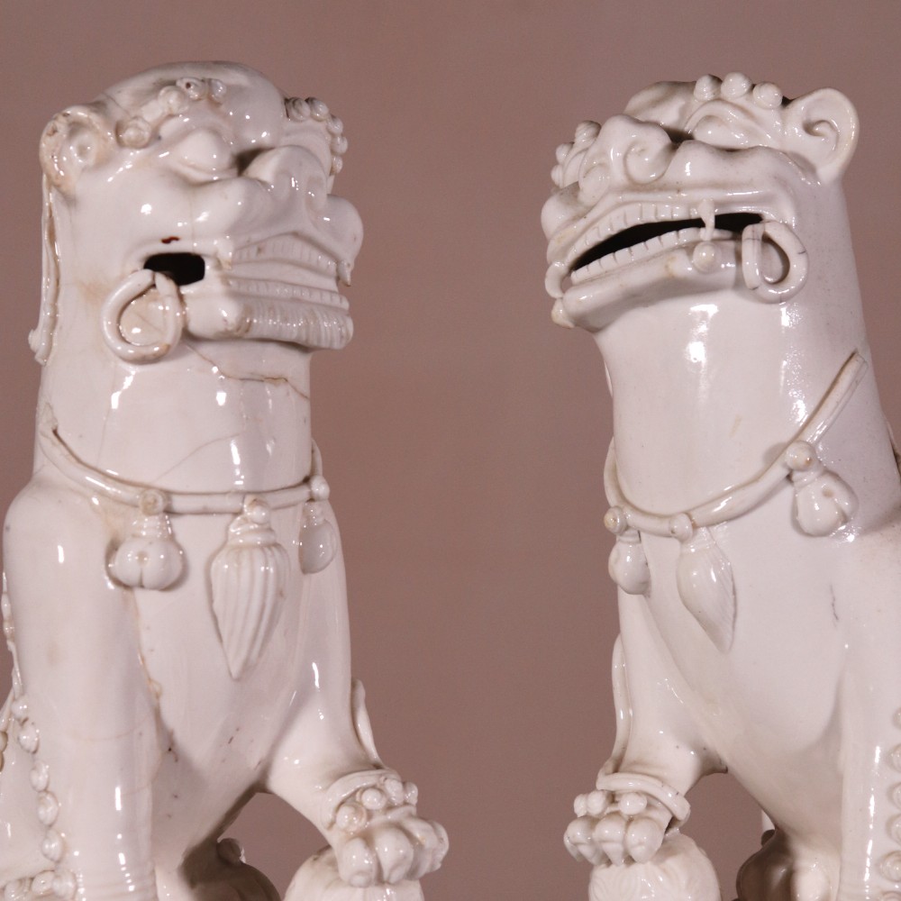 A pair of 18th-century cream-glazed Blanc de Chine porcelain guardian lion statues seated upright on rectangular bases. View III
