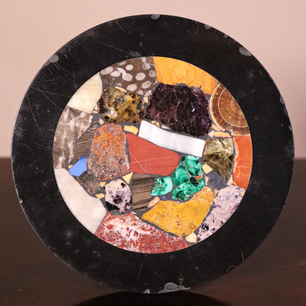 A nineteenth-century Ashford black marble miniature table featuring a round top inlaid with colourful geometric marble specimens, supported by a turned baluster column on a square plinth base. View IV