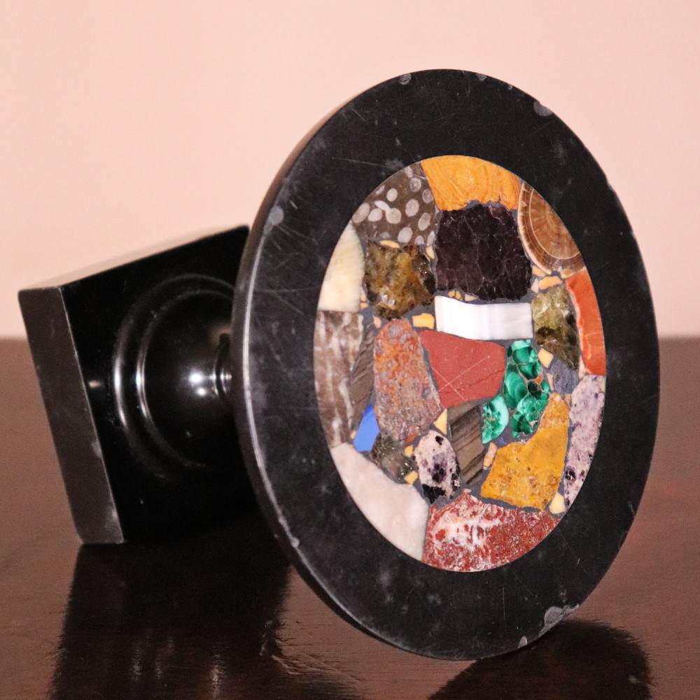 A nineteenth-century Ashford black marble miniature table featuring a round top inlaid with colourful geometric marble specimens, supported by a turned baluster column on a square plinth base. View V