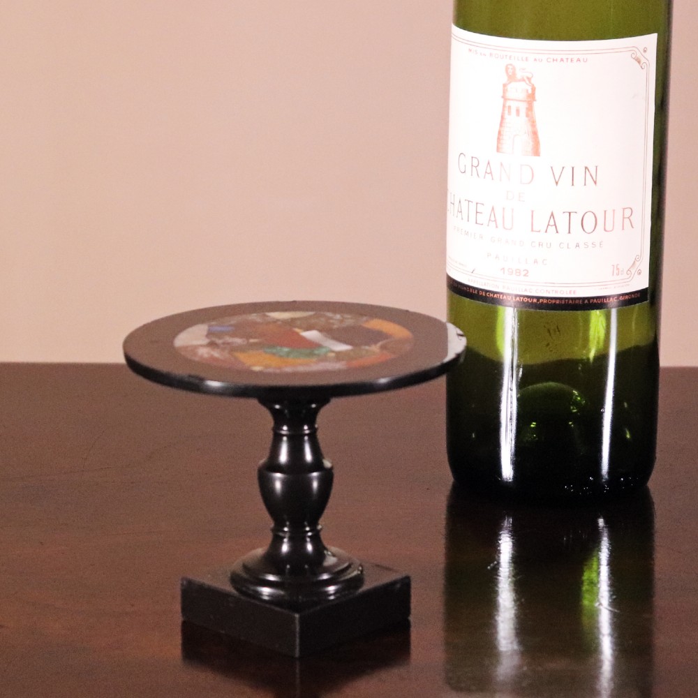 A nineteenth-century Ashford black marble miniature table featuring a round top inlaid with colourful geometric marble specimens, supported by a turned baluster column on a square plinth base. View VII