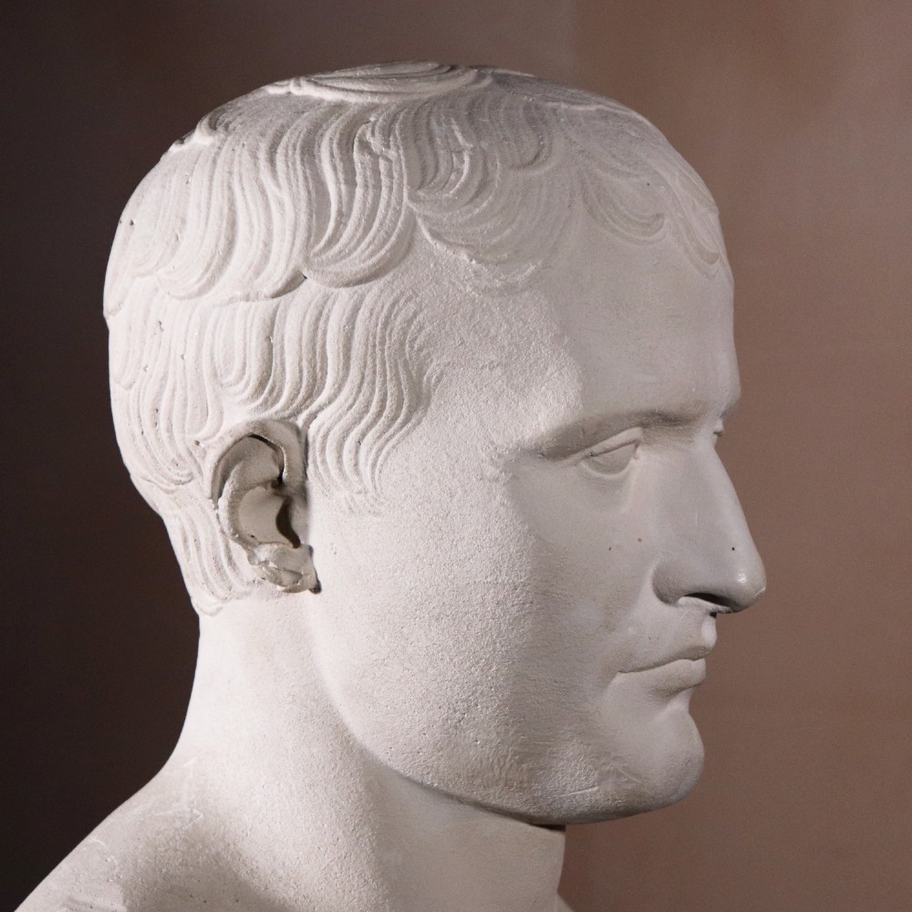 An off-white plaster portrait bust depicting Napoleon Bonaparte with short classical hair and a square pedestal base. View V