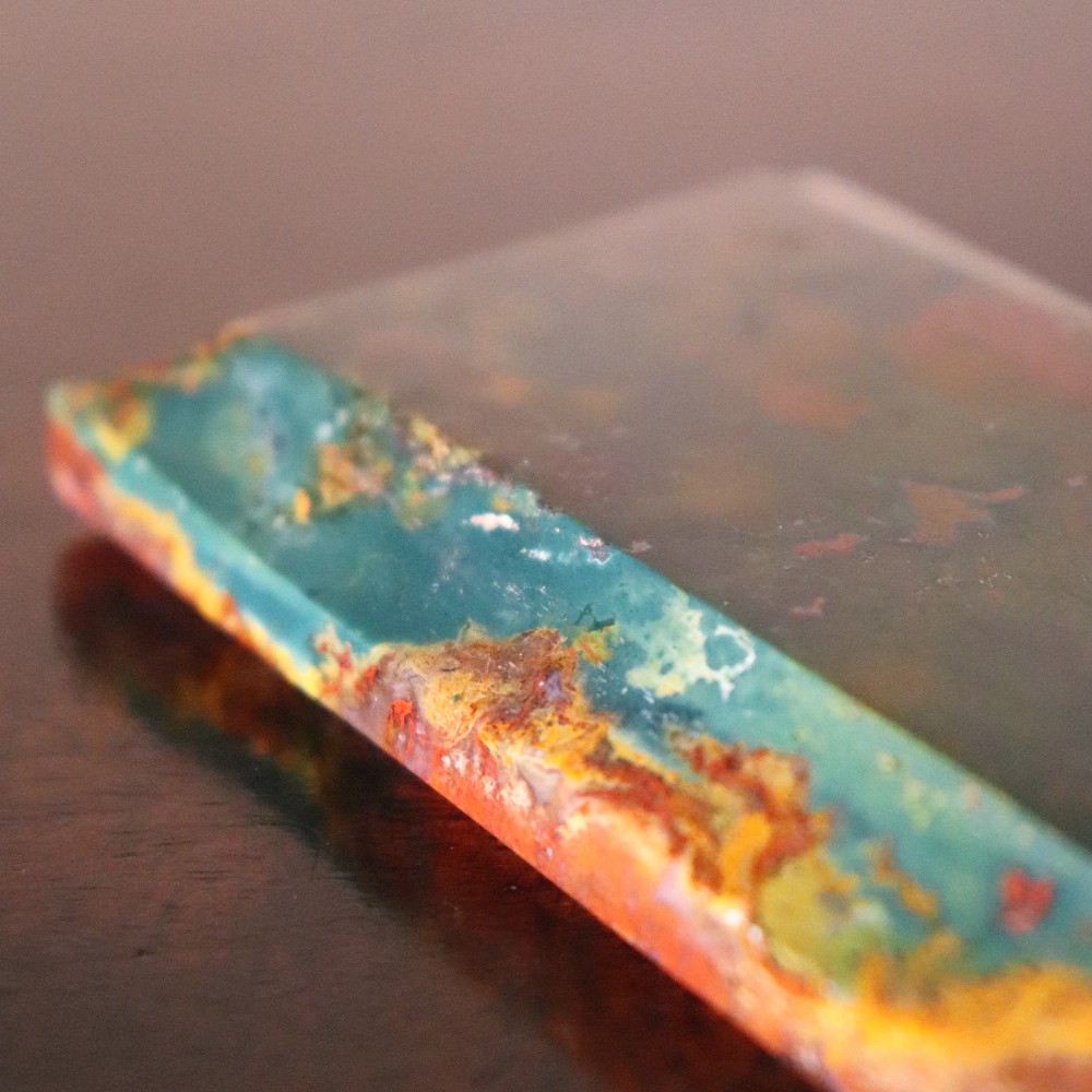 A rectangular nineteenth-century agate paperweight featuring bevelled edges and a mottled surface of deep green, ochre, and rust red tones. View IV