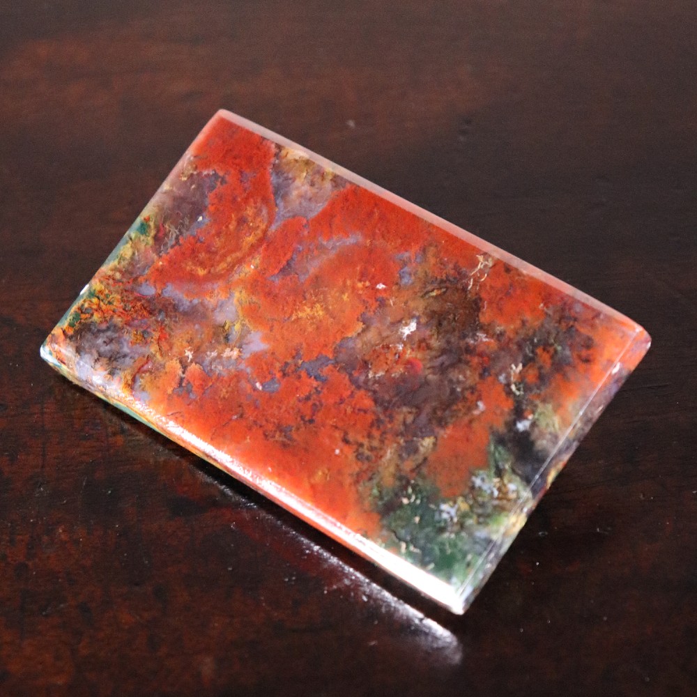 A rectangular nineteenth-century agate paperweight featuring bevelled edges and a mottled surface of deep green, ochre, and rust red tones. View VI