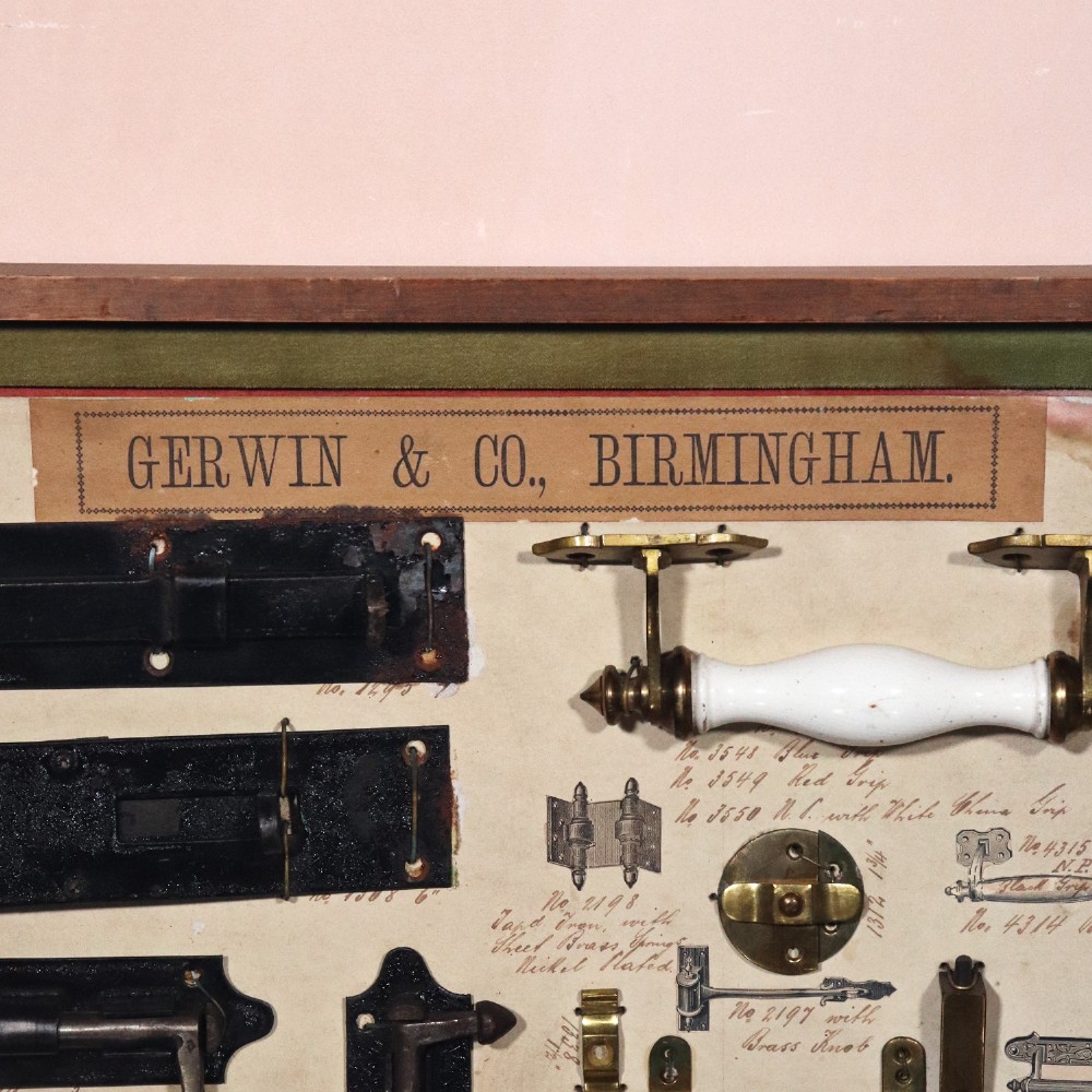 A framed commercial sample board containing antique brass and cast iron door hardware, latches, and ceramic handles mounted on annotated paper with a header reading Gerwin & Co., Birmingham. View II