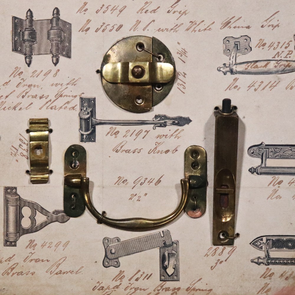 A framed commercial sample board containing antique brass and cast iron door hardware, latches, and ceramic handles mounted on annotated paper with a header reading Gerwin & Co., Birmingham. View III