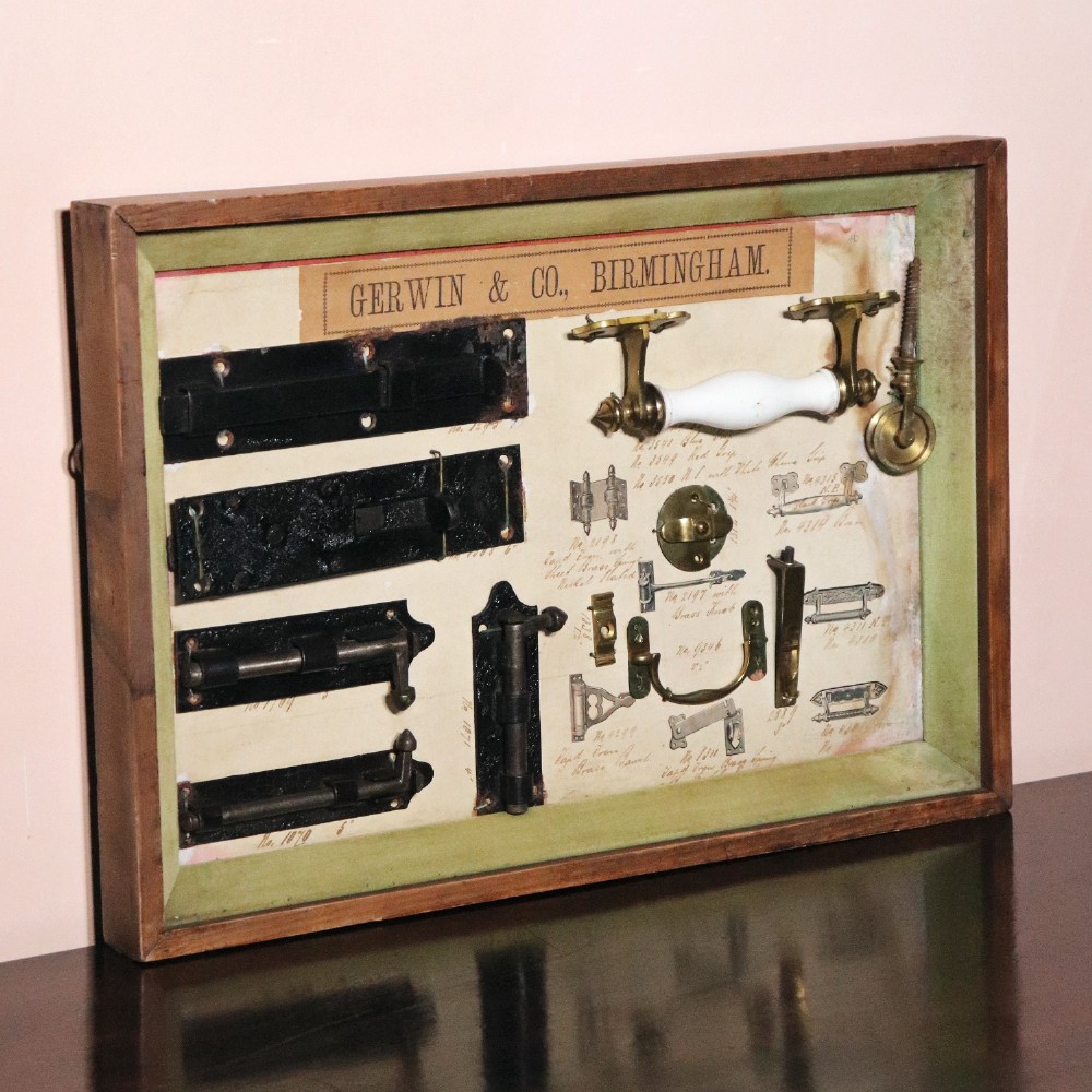 A framed commercial sample board containing antique brass and cast iron door hardware, latches, and ceramic handles mounted on annotated paper with a header reading Gerwin & Co., Birmingham. View V