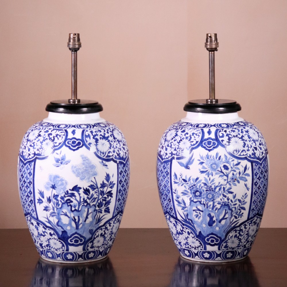 A pair of Chinese style blue and white porcelain ginger jar table lamps featuring floral panels mounted on dark wooden bases.