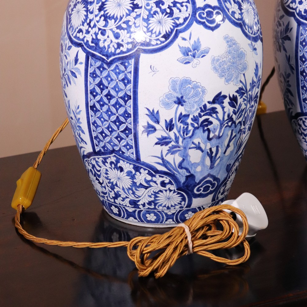 A pair of Chinese style blue and white porcelain ginger jar table lamps featuring floral panels mounted on dark wooden bases. View VII