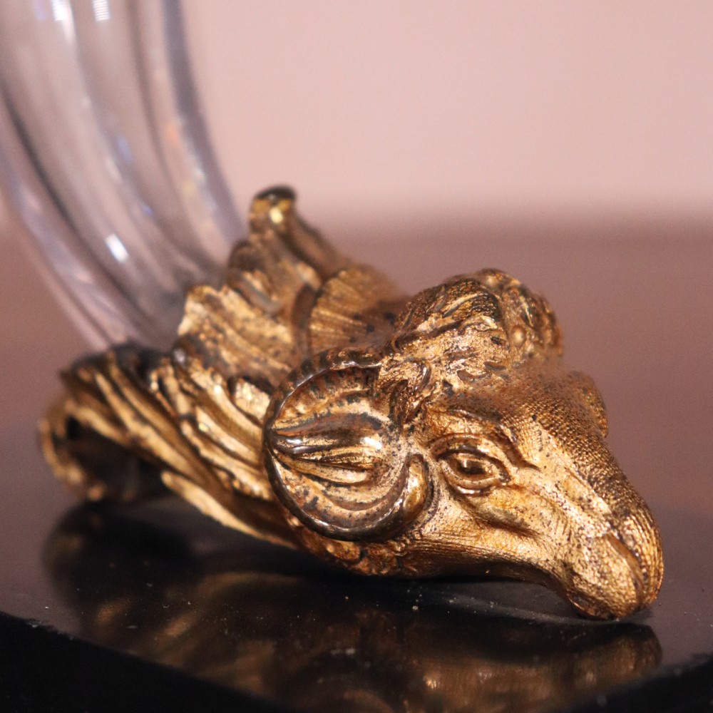 A pair of Regency cornucopia vases featuring fluted clear glass horns set into gilt bronze rams head mounts on rectangular black marble bases. View II
